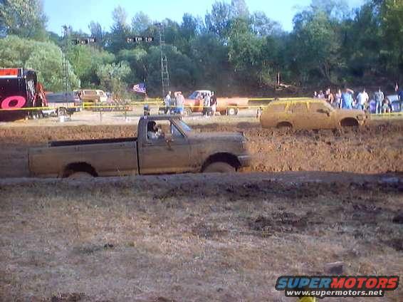 Truck stuck in mud, another SUV stuck in mud behind it, people watching