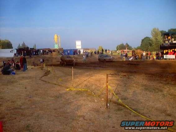 Mud run event with vehicles and crowds, yellow caution tape on ground