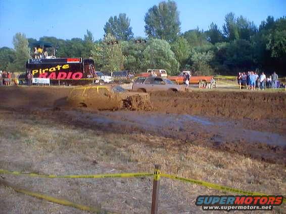 Muddy truck stuck in a mud pit with a "Pirate Radio" truck in the background