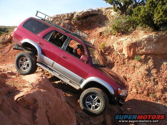 1996 Toyota 4Runner climbing a steep, rocky hill. The vehicle has a roof rack and aftermarket wheels