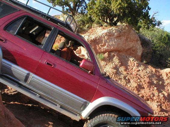 Red SUV climbing rocky terrain, driver visible inside