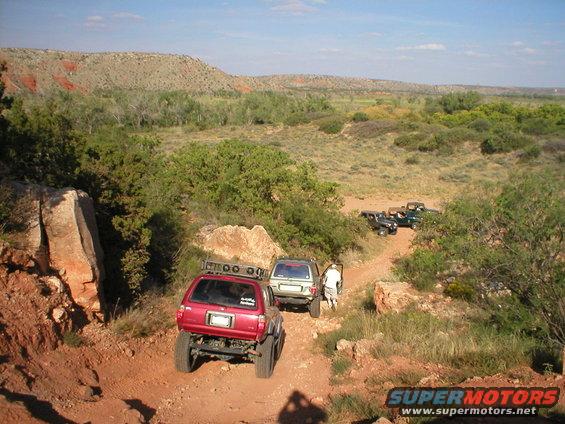Red 1996 Toyota 4Runner rear view on a dusty trail with other SUVs behind