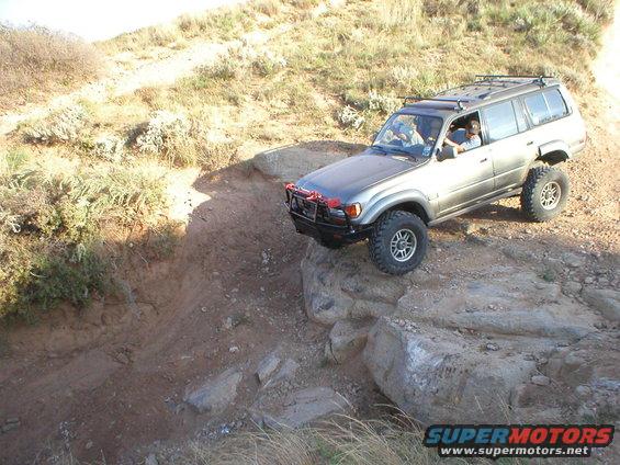 Silver Toyota Land Cruiser off-roading on rocks, front bumper modified with a winch guard