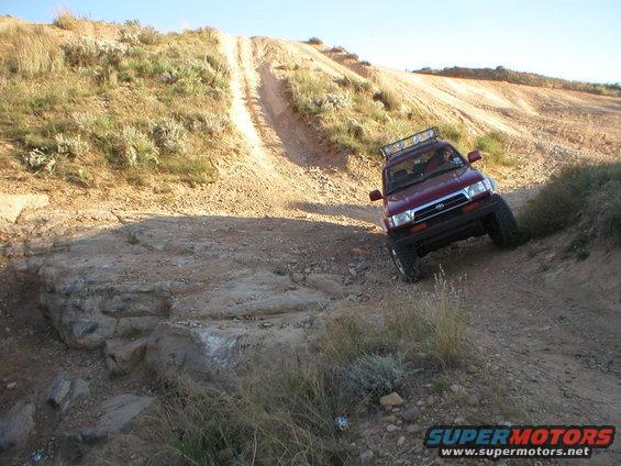 Maroon 1996 Toyota 4Runner driving on a steep dirt trail with rocky terrain
