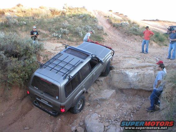 Silver Toyota Land Cruiser navigating a rocky off-road trail with people watching