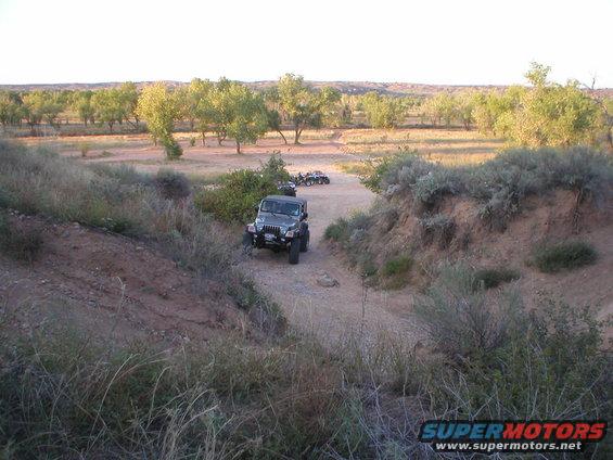Dark gray Jeep Wrangler on dirt road, with ATVs in background