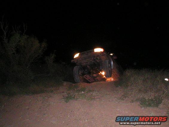 1996 Toyota 4Runner tilted on its side at night, headlights on, on a dirt path