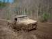 1978 Ford Bronco - Truck stuck deep in mud on a wooded trail, driver visible.