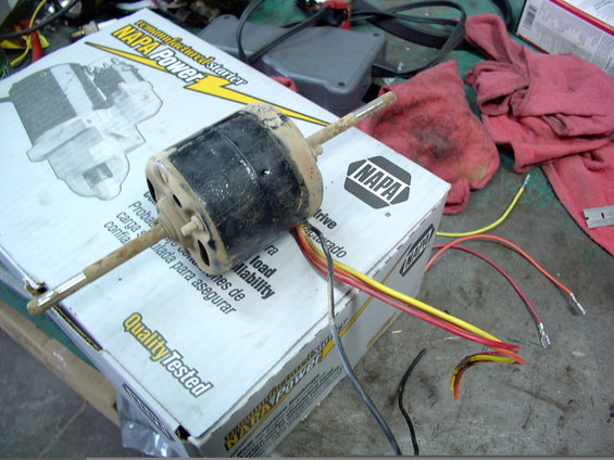 Blower motor with wires on a NAPA box. Red rags and tools are visible
