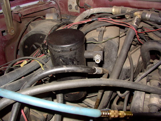 Engine bay with black cylindrical component, hoses, and wiring