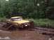 1978 Ford Bronco - A yellow pickup truck navigates a muddy track, kicking up a large spray of mud.