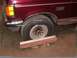 1988 Ford C-350 (Centurion Conversions) - Maroon Ford F-Series truck front fender and wheel. A metal alignment tool rests on blocks under the tire.