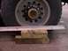1988 Ford C-350 (Centurion Conversions) - A close-up view of a heavy-duty truck wheel supported by wooden blocks and a metal bar.