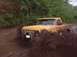 1978 Ford Bronco - A yellow pickup truck navigates a muddy terrain, kicking up a large spray.