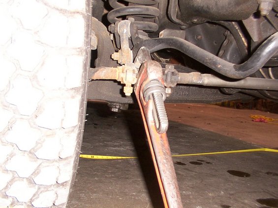 Close-up of vehicle's front suspension and steering linkage with a large wrench on a tie rod end