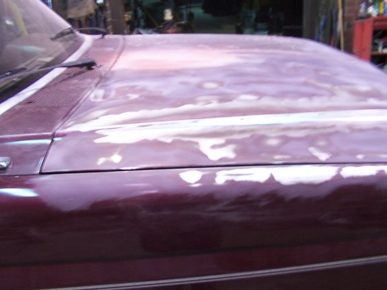 Car hood showing primer patches over maroon paint, with windshield wipers visible