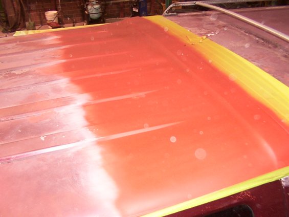 Vehicle roof with red primer and yellow masking tape, ready for paint