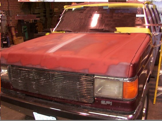 Front view of a maroon Ford F-Series truck with a red hood, undergoing paint prep. Grille and headlights visible