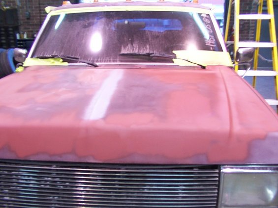 Red truck hood with primer, chrome grille, and taped windshield. Visible text on windshield reads '1988-1991'