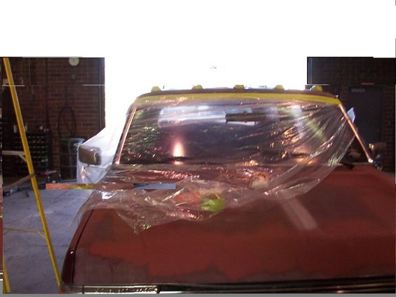 Front of a truck cab covered in plastic sheeting, likely for painting. A ladder is visible to the left