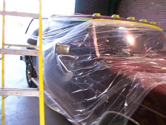 Side and front of a dark-colored truck covered in plastic sheeting, with a ladder nearby