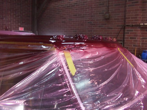 Vehicle roof covered in red paint and plastic sheeting, with yellow tape