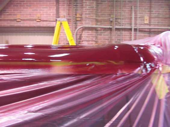 Red automotive part covered in plastic sheeting, with a yellow ladder in the background
