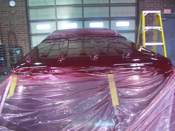 Red vehicle roof covered in plastic sheeting, with chrome trim visible