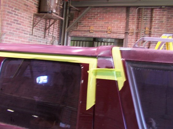Close-up of a vehicle's maroon roofline and window frame, masked with yellow tape