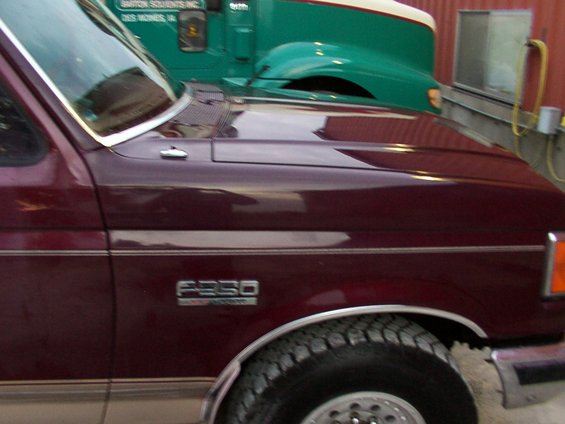 Maroon Ford F-250 pickup truck fender and hood, with a green truck behind it