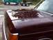 1988 Ford C-350 (Centurion Conversions) - Close-up of the hood and fender of a maroon vehicle, showing reflections of trees and clouds. A green truck is in the background.