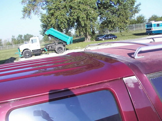Red SUV roof rack, side view. Dump truck and car in background