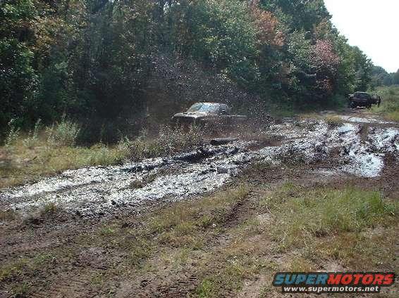 Truck driving through a muddy trail, kicking up a lot of water and mud