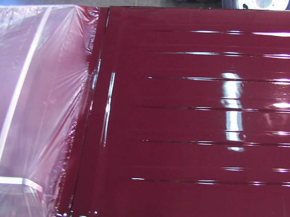 Red painted roof panel with horizontal ridges, covered in plastic sheeting on the left