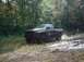 1978 Ford Bronco - A black pickup truck is stuck in the mud, kicking up spray as it attempts to move.