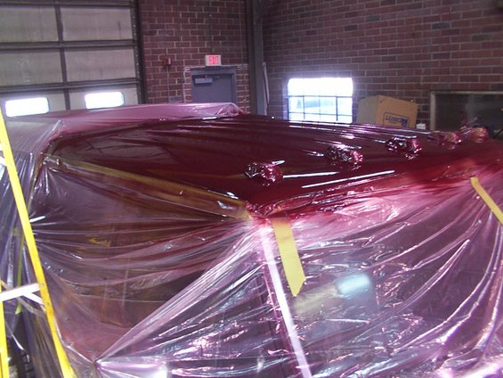 Vehicle roof covered in red liquid and plastic sheeting, inside a garage