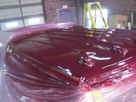 Maroon car hood covered in plastic wrap, showing fresh paint and chrome trim