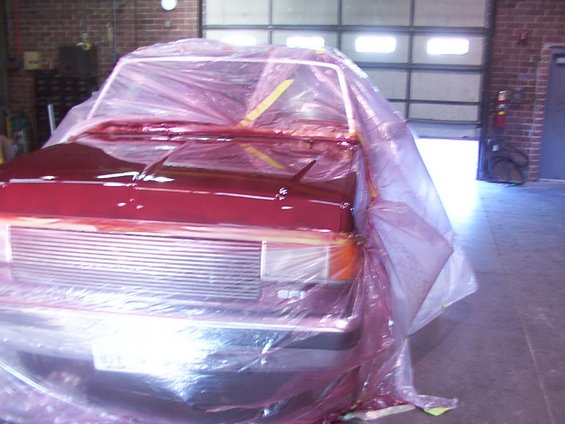 Red truck front end covered in plastic, being painted. 1988 Ford C-350 (Centurion Conversions) is not visible