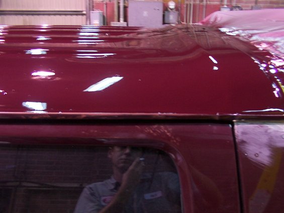 Maroon vehicle roof with visible ripples and a reflection of a person