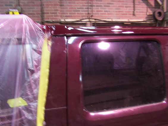 Side view of a maroon vehicle's rear window and roofline, covered in plastic sheeting and masking tape