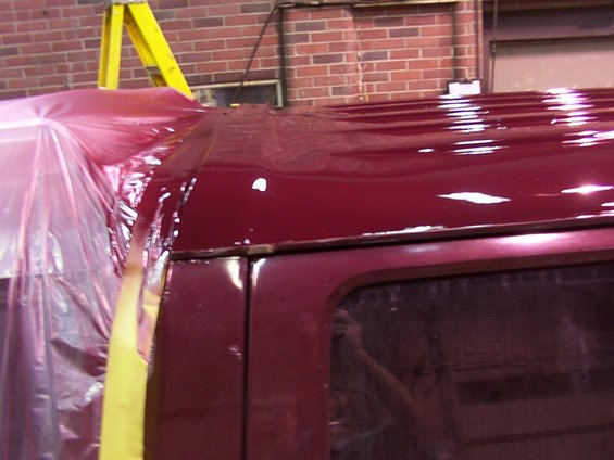 Maroon vehicle roof covered in plastic sheeting and tape, with a yellow ladder in the background