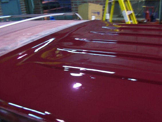 Maroon vehicle roof with horizontal ridges, showing reflections and a section of unfinished red primer