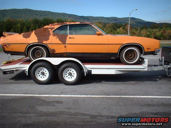Orange 1970 Mercury Cyclone coupe with significant rust on the rear quarter panel, on a white trailer
