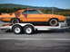 1970 Mercury Cyclone - A rusty orange 1970 Mercury Cyclone coupe is transported on a trailer, showing its side profile against a backdrop of trees and mountains.