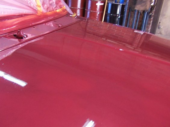 Close-up of a shiny red vehicle hood with some plastic sheeting over the windshield area