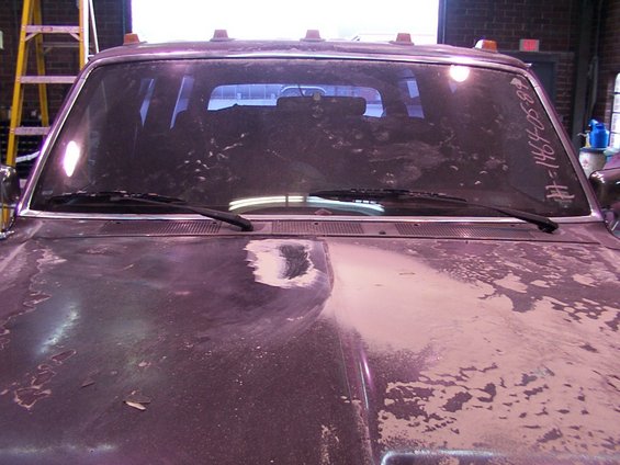 Truck hood with peeling paint and a dirty windshield. Text '#=1464-05-89' is written on the windshield