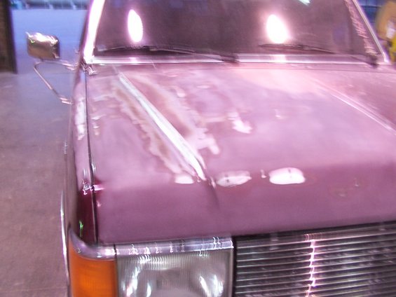 Close-up of a vehicle hood with primer and body filler, showing damage and repair work