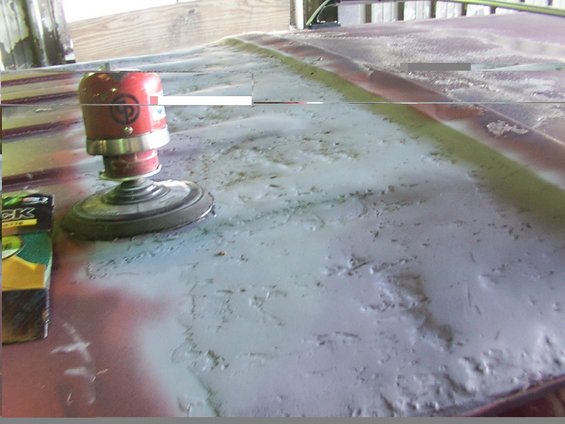 Orbital sander on a vehicle roof being prepped for paint. A box of sandpaper is nearby