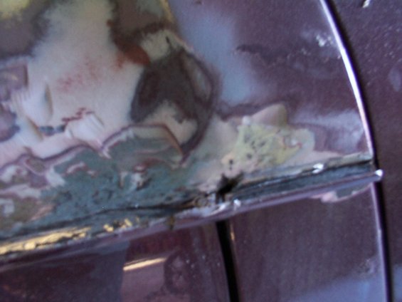 Close-up of auto body damage showing rust and primer on a dark purple vehicle