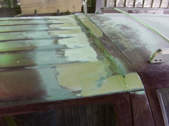 Roof bodywork with primer and filler on a dark red vehicle